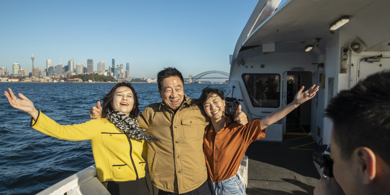 3 students on a boat posting for a photo with Sydney City in the distance