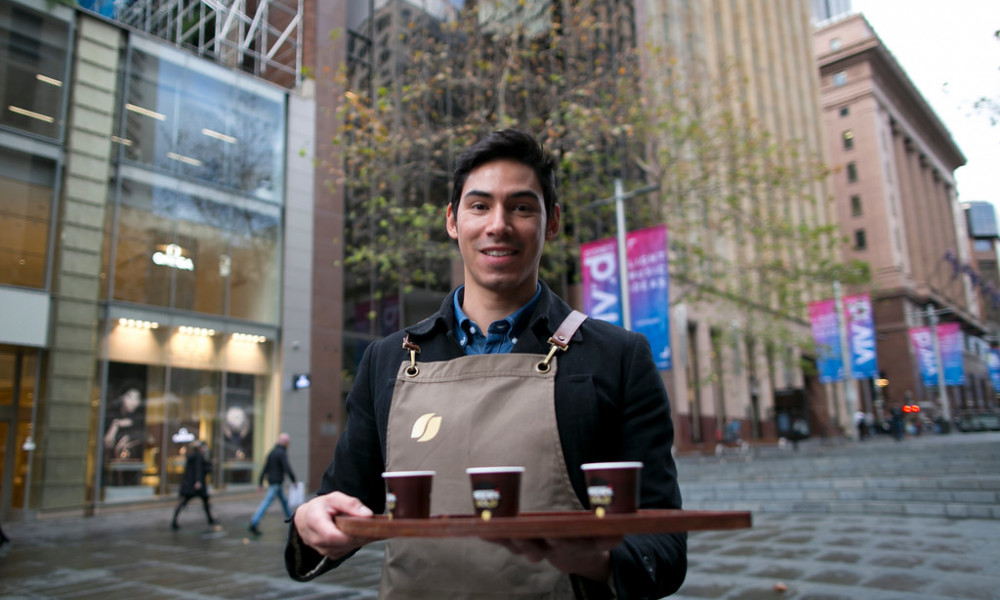 Barista smiling whilst holding coffee in Sydney CBD.