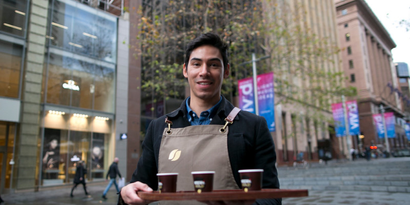 Barista smiling whilst holding coffee in Sydney CBD.